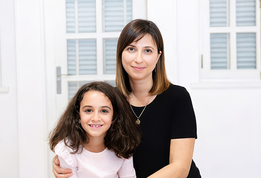 BYU-Pathway student Alina Ambariani from Georgia sits with her daughter at home, smiling together for a warm family portrait.