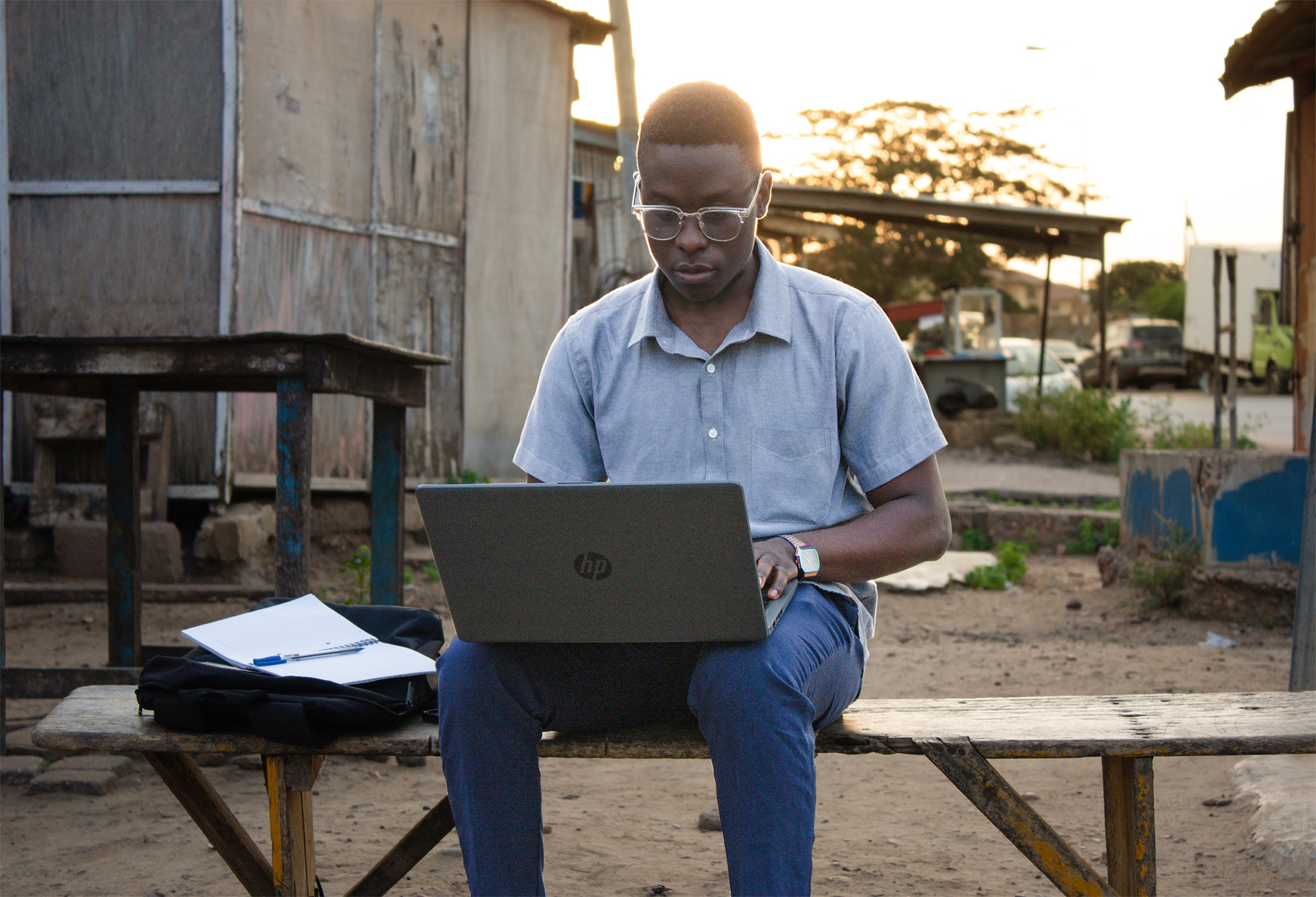Man working on a computer sitting on an outdoor bench.