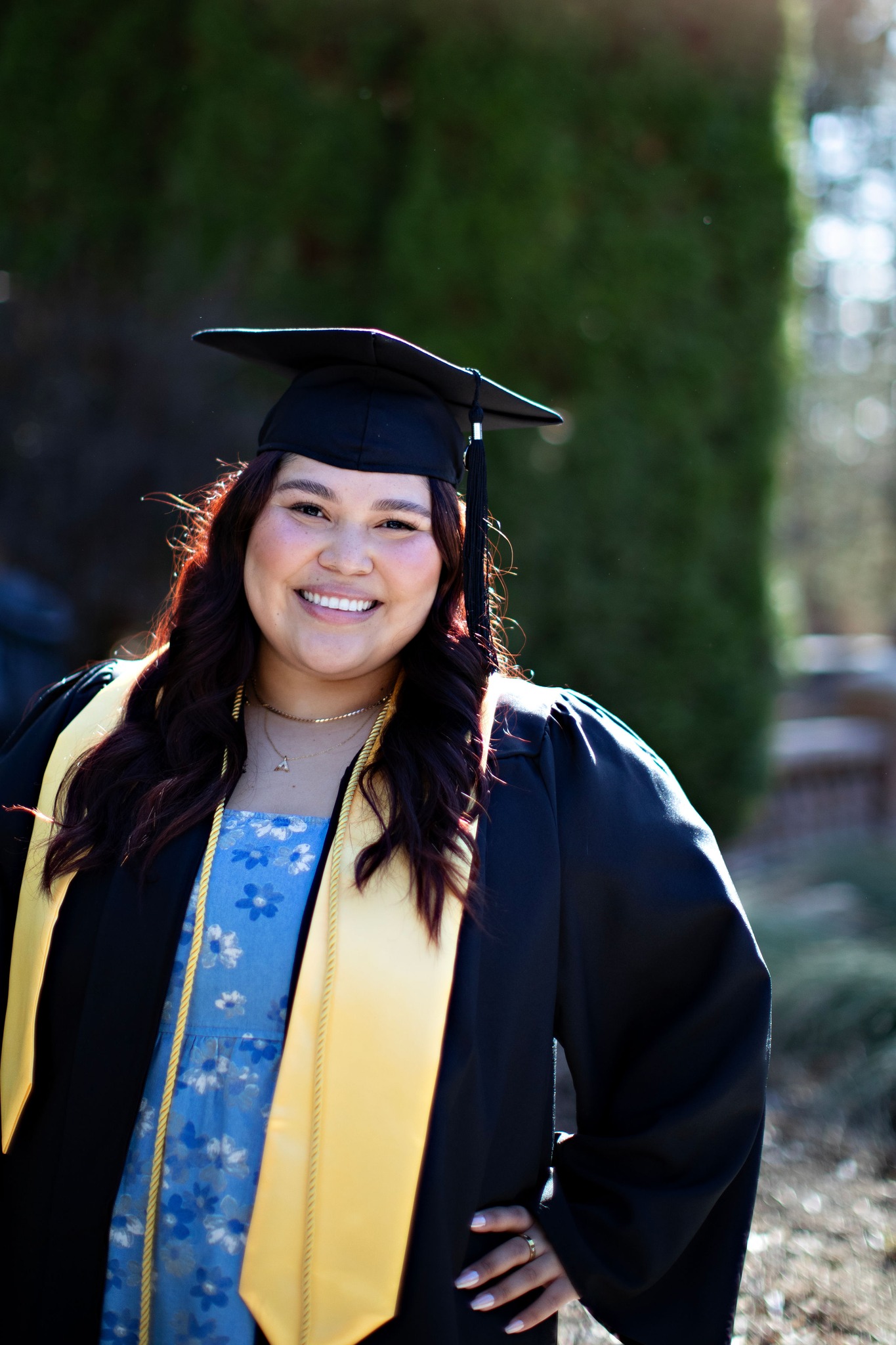 BYU-Pathway graduate Ale Angulo smiles in cap and gown while holding a bouquet of flowers outdoors.