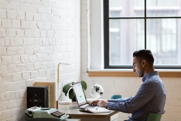 Man sits at a desk near a window working on a laptop