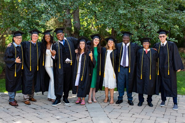 A group of BYU-Pathway graduates stand with their arms around one another, each wearing a cap and gown.