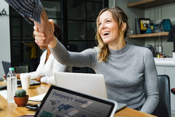 Woman shakes hand seated with a laptop