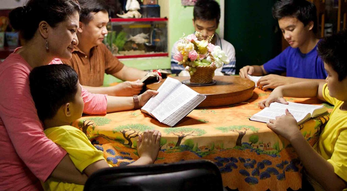 A woman reads scriptures at a table with her husband and children as part of her church online degree