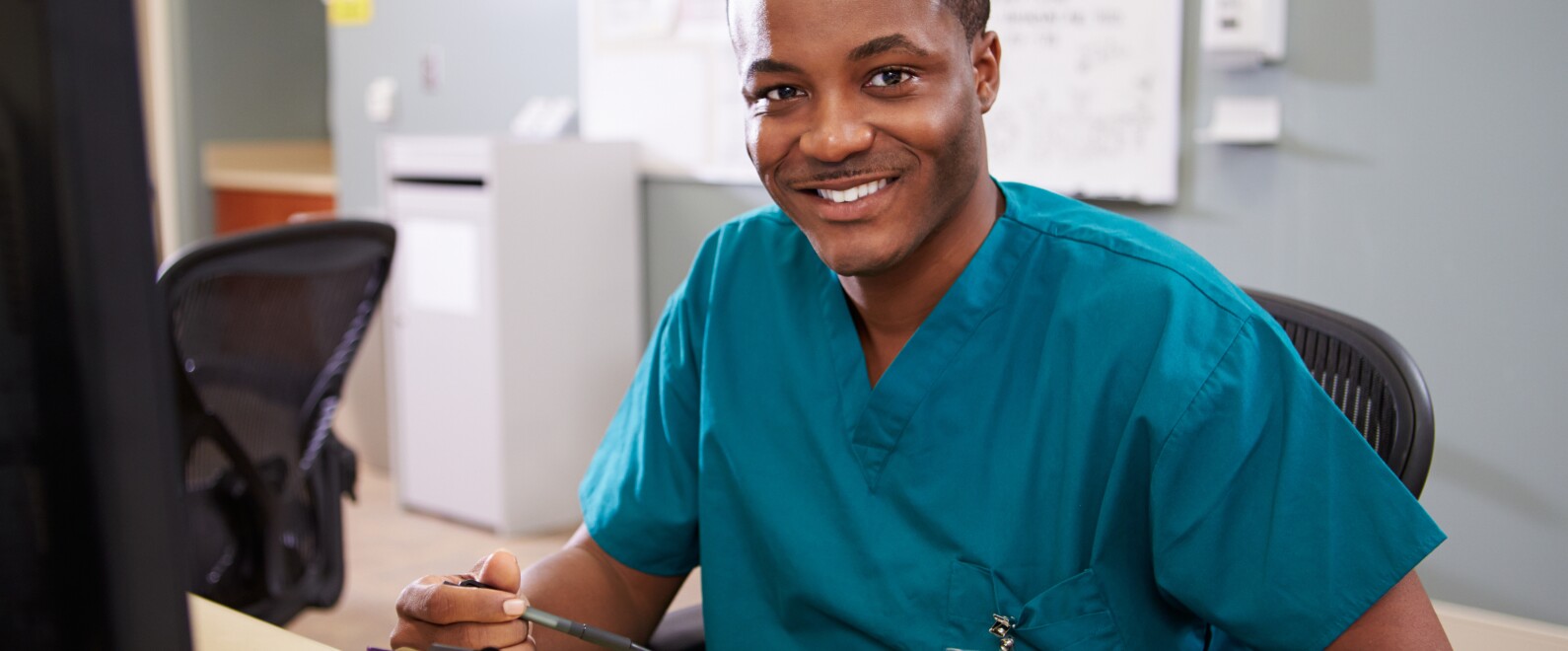 Portrait Of Male Nurse Working At Nurses Station