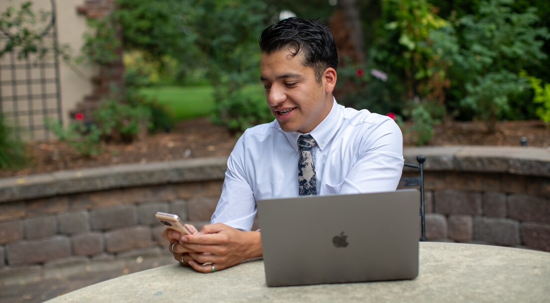 Young man using his phone and laptop as he takes online courses to earn a bachelor's degree in three years through BYU-Pathway Worldwide.