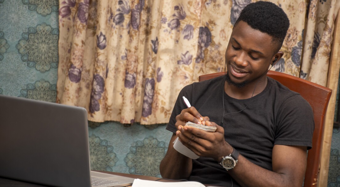 young african student receiving lectures online, taking notes