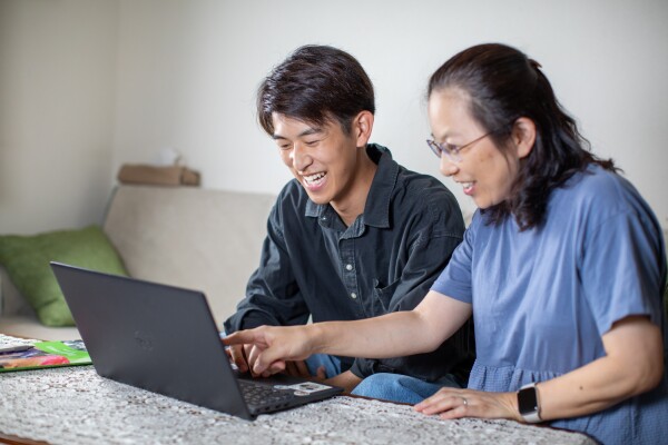 A man and woman smiling as they watch a devotional on a laptop.