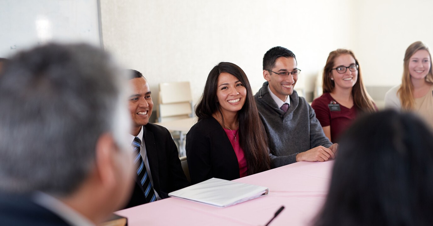 A teacher sits at a table, leading a council meeting