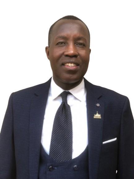 A man wearing a suit jacket and tie stands smiling
