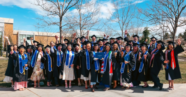 A large group of BYU-Pathway graduates cheer as they stand outside together, dressed in the ceremonial graduation attire