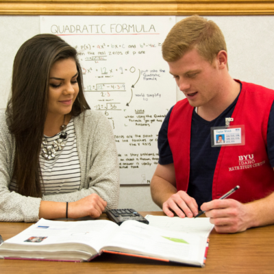 A male tutor reading through a textbook with a female student.