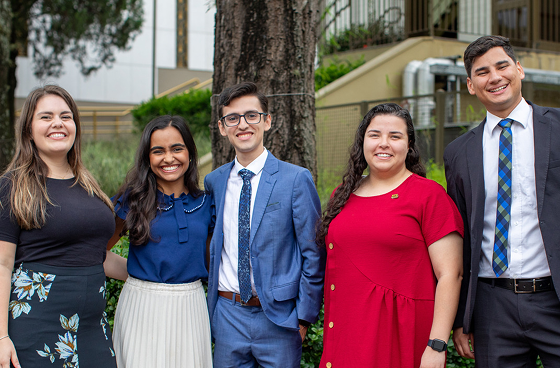 Five BYU-Pathway students in Brazil stand together outdoors, smiling in professional attire near campus greenery and buildings.